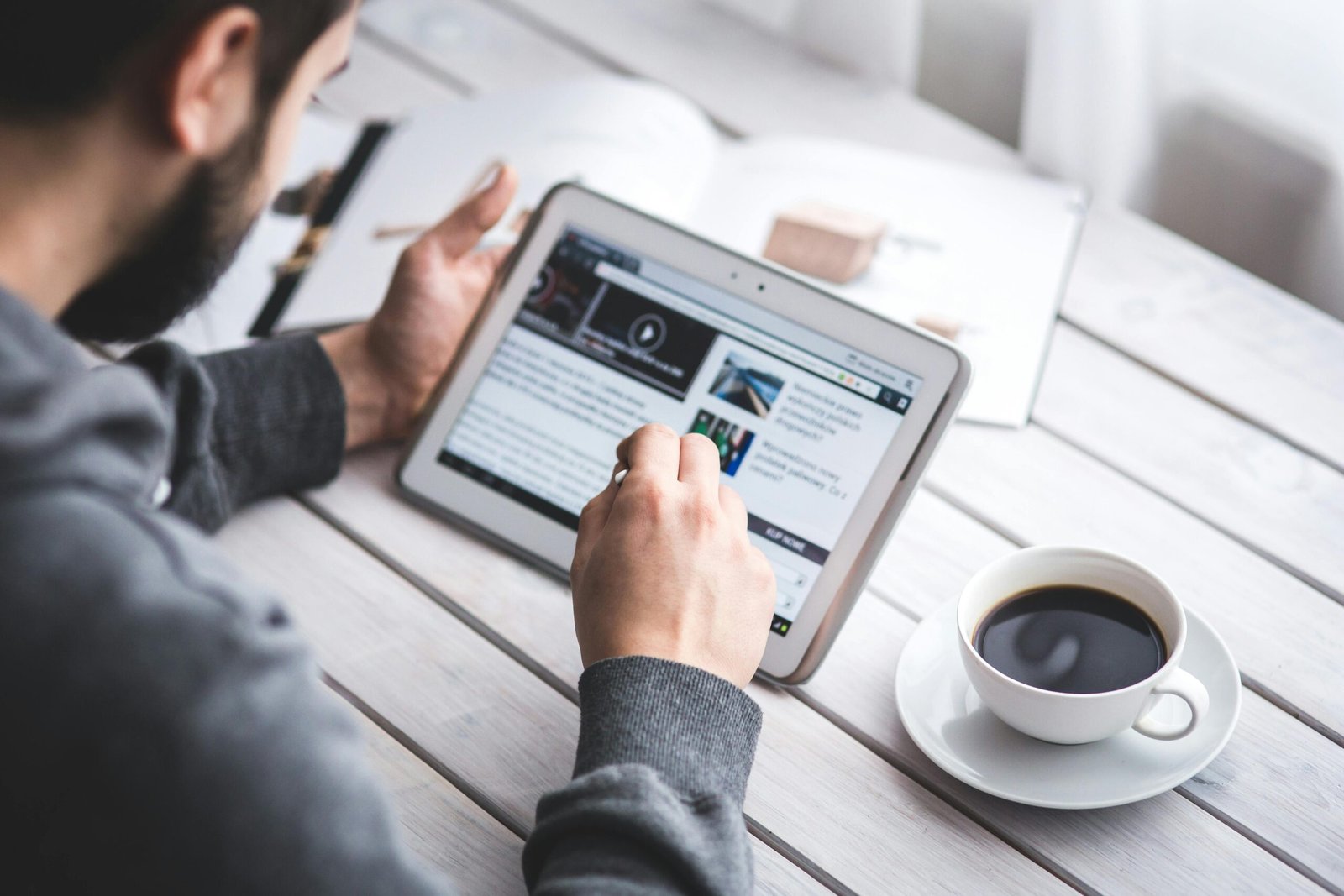 A man uses a tablet to browse news while enjoying a cup of coffee, stylus in hand.