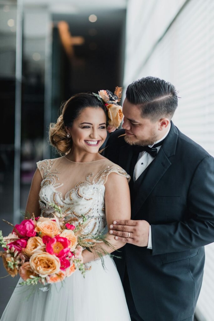 Joyful wedding portrait of a young couple indoors, holding a vibrant bouquet.