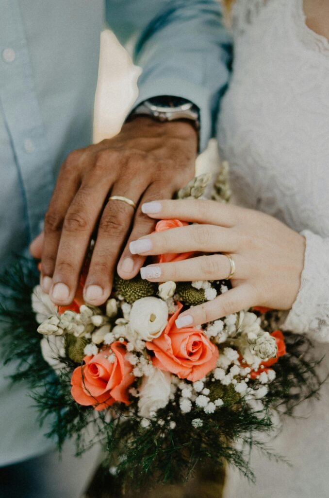 Hands of the bride and groom with wedding rings and floral bouquet, symbolizing love and commitment.