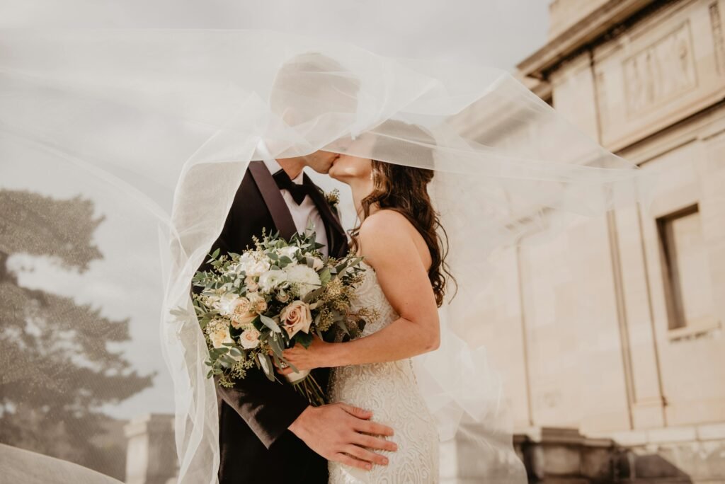 Bride and groom share a tender kiss under a veil, showcasing love and romance on their special day.