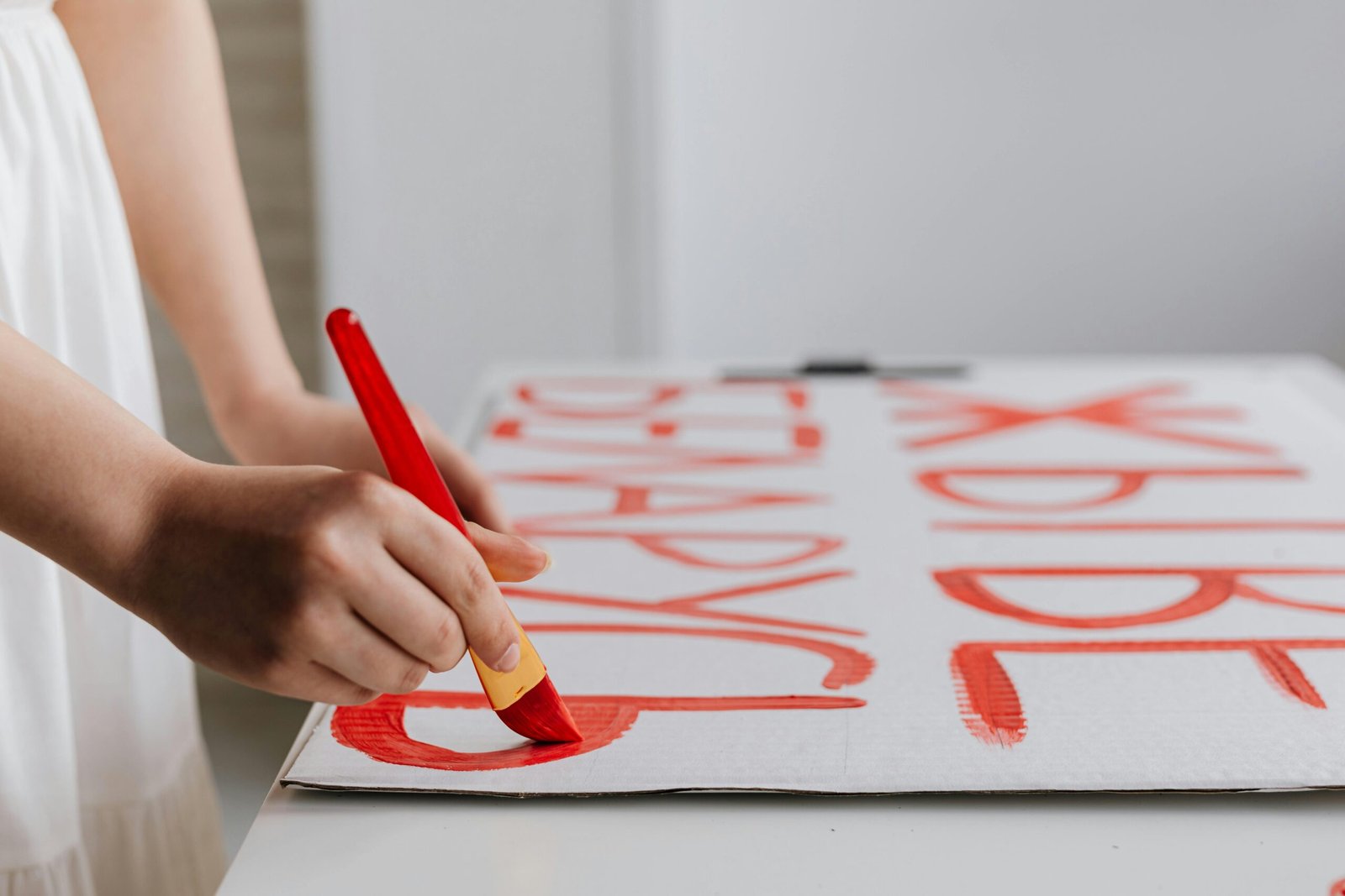 A person paints a protest placard with red paint, emphasizing bold letters.